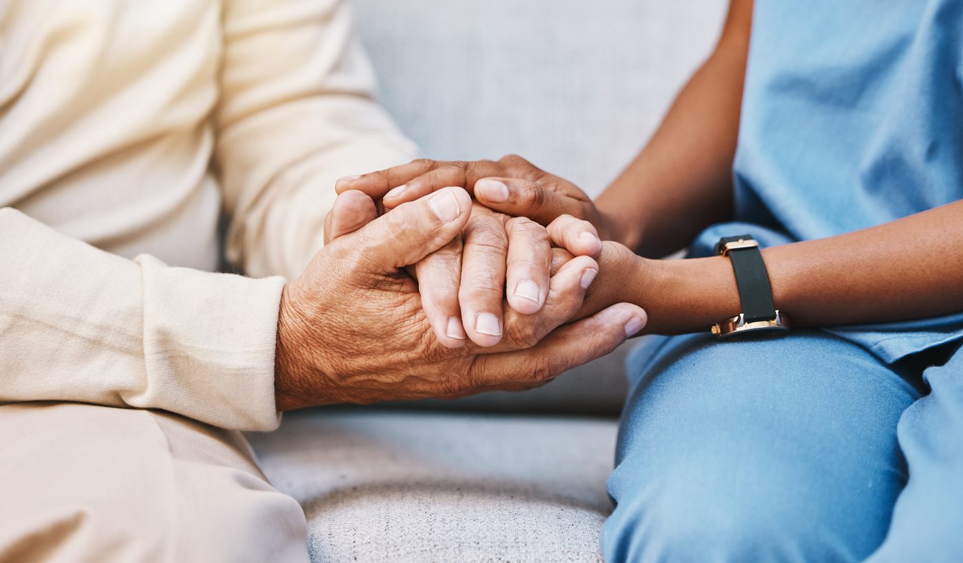 Older person holding hands with a healthcare worker wearing blue scrubs and a black watch.