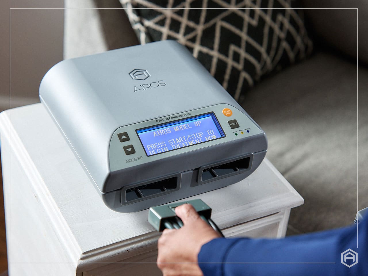 Hand holding a control connected to an AIROS Model 8P sequential compression device on a white table.