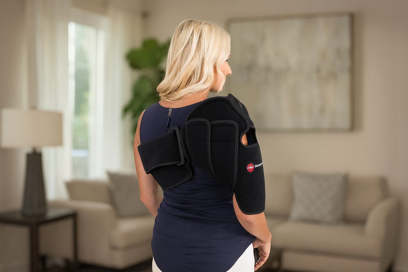 Woman wearing a black shoulder brace in a living room setting.