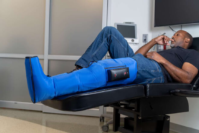 Man lying on a medical exam table with a blue compression therapy sleeve on his leg.