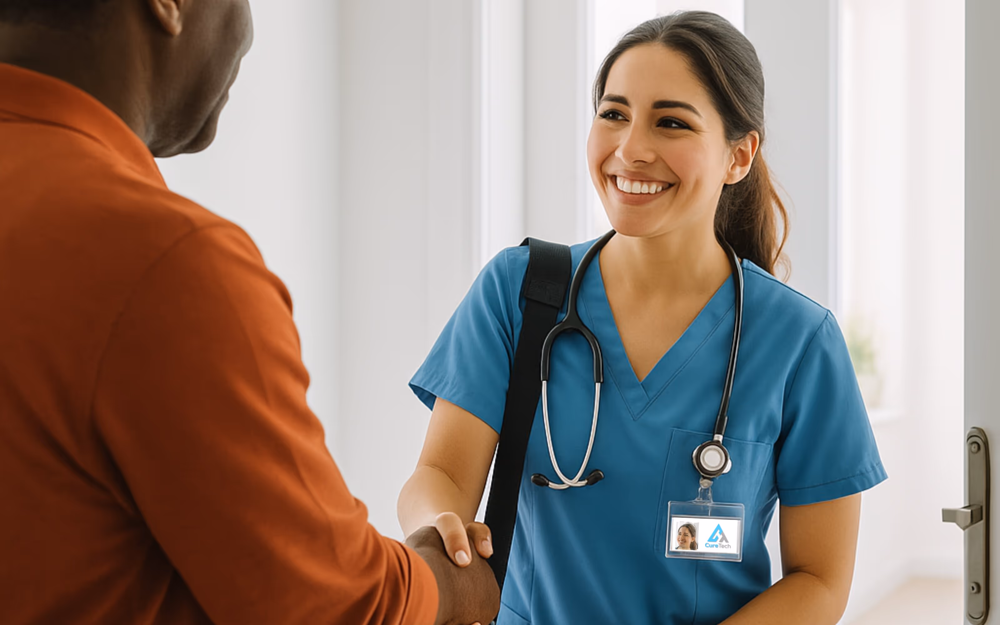 Smiling nurse in blue scrubs shaking hands with a man wearing an orange shirt at a doorway.