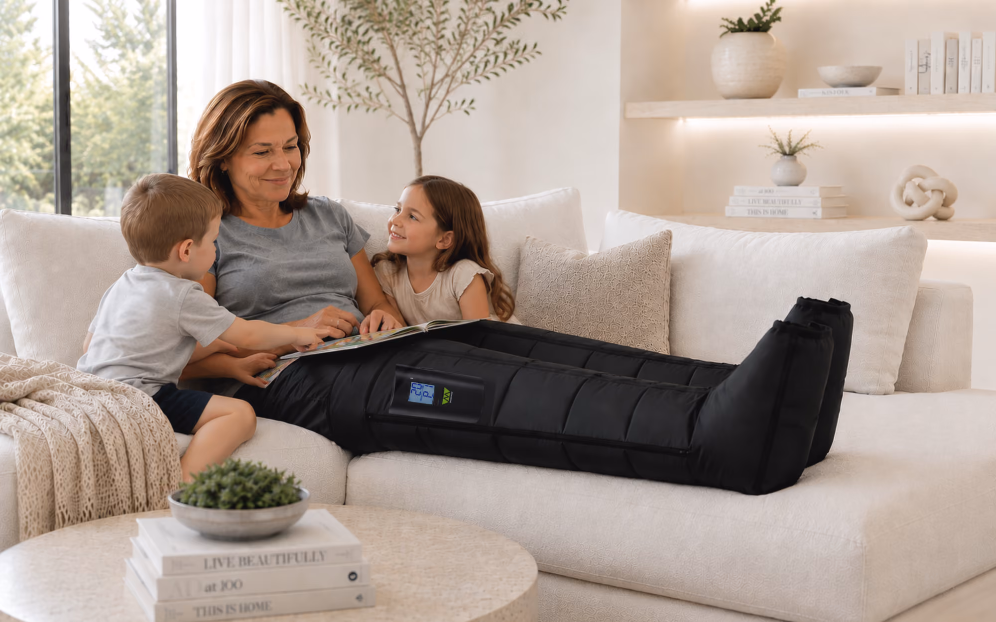 Woman wearing black leg compression sleeves sitting on couch reading with two children.