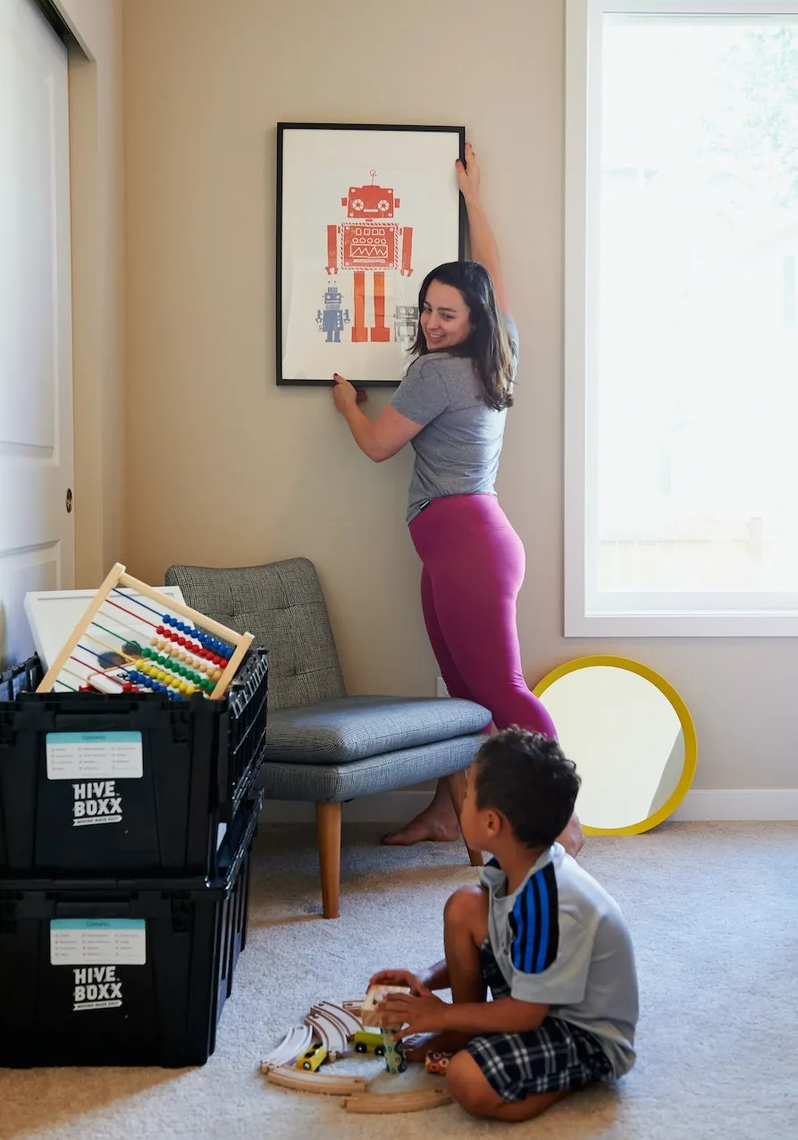 Mother showing her kid a picture frame as she puts it on a wall.