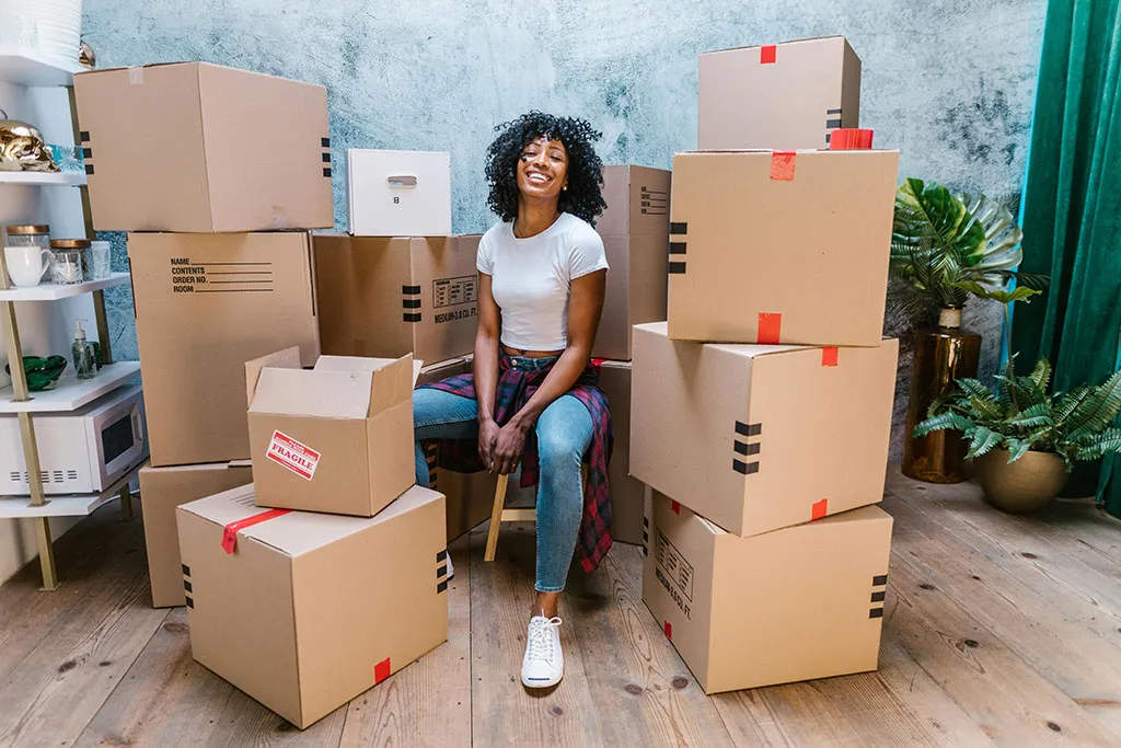 Young woman sitting happy in the middle of a stack of moving boxes.