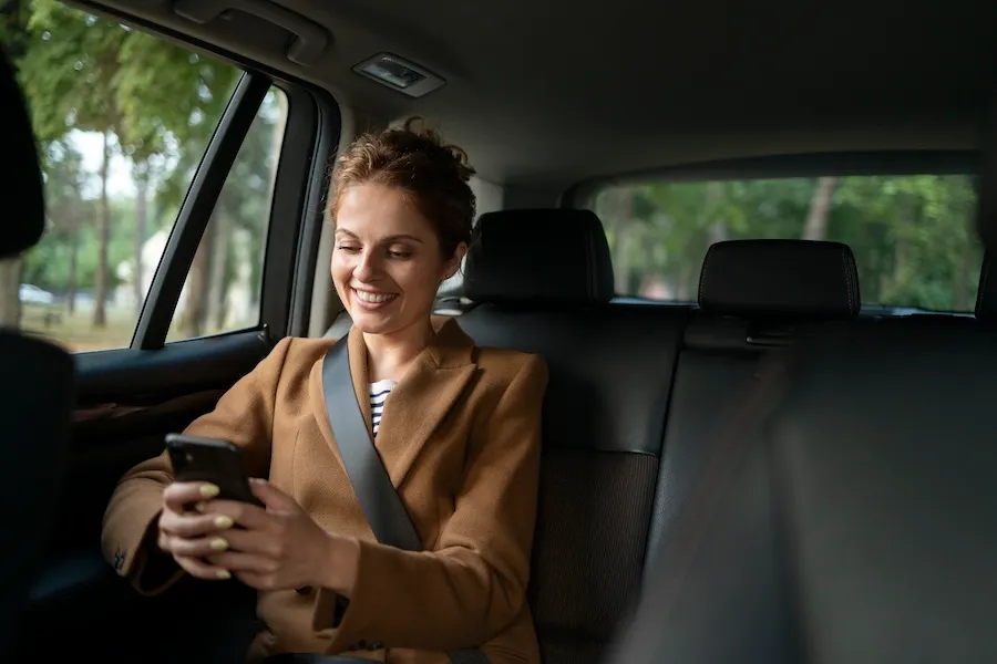Woman in the back seat of a taxi cab texting on her mobile phone.