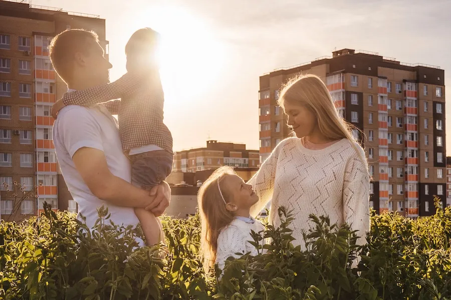 Family in the park, at sunset, with apartment building in the back.