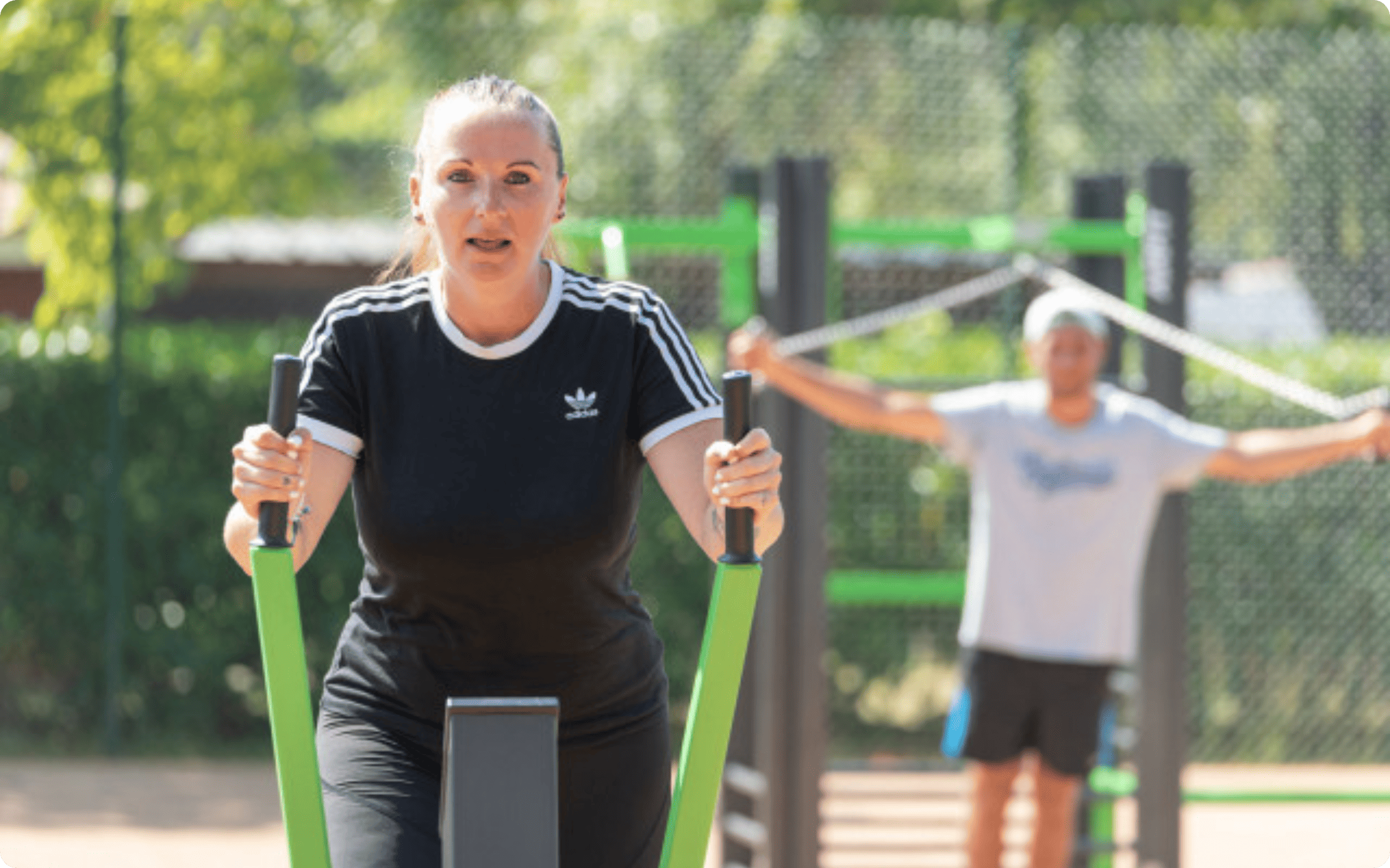 Outdoor fitness park with blue exercise equipment on artificial grass and houses in the background.