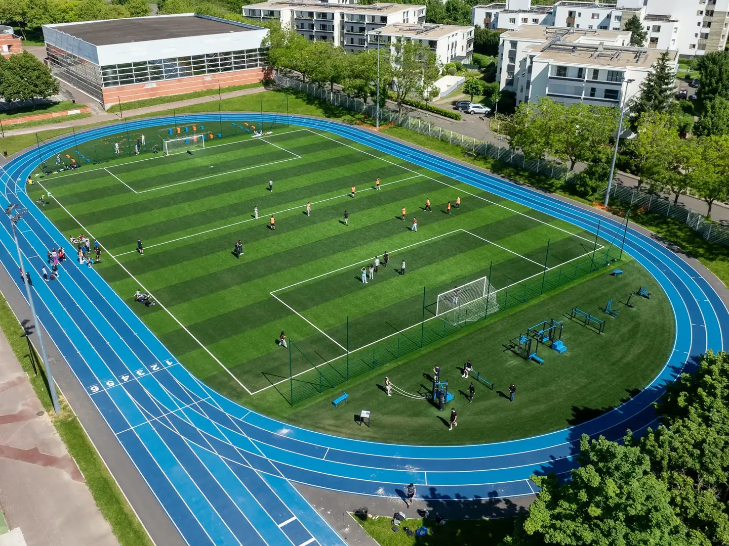 Vue aérienne du stade Pierre de Coubertin à Montigny-le-Bretonneux : piste d'athlétisme bleue, terrain de football et plateau de cross-training AirFit dans le virage