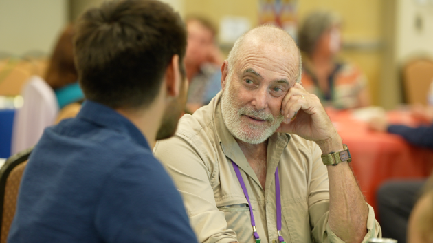 Older man with white beard engaged in conversation with younger man in an indoor social setting.