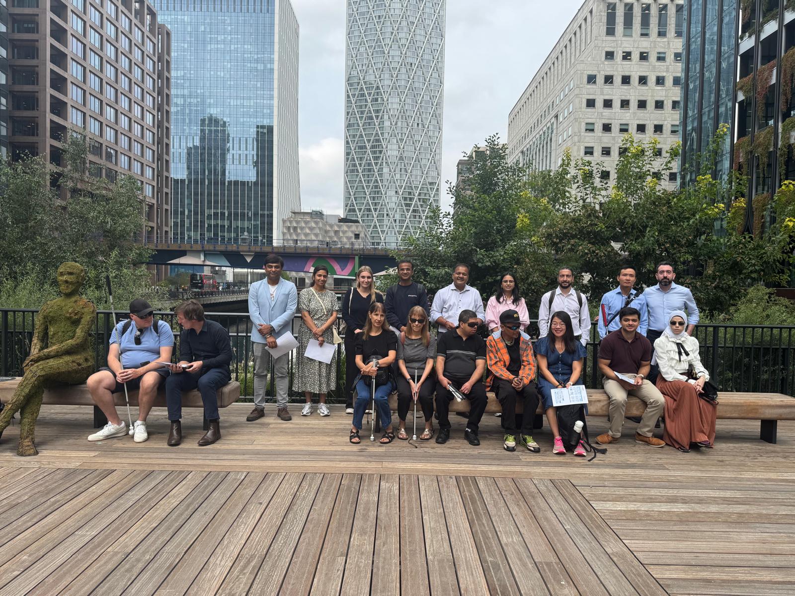 All the participants are posing for the camera together with Ishan and Krinal form the Travel Hands team included. The beautiful Canary Wharf background is visible in the picture with big buildings and greenery.