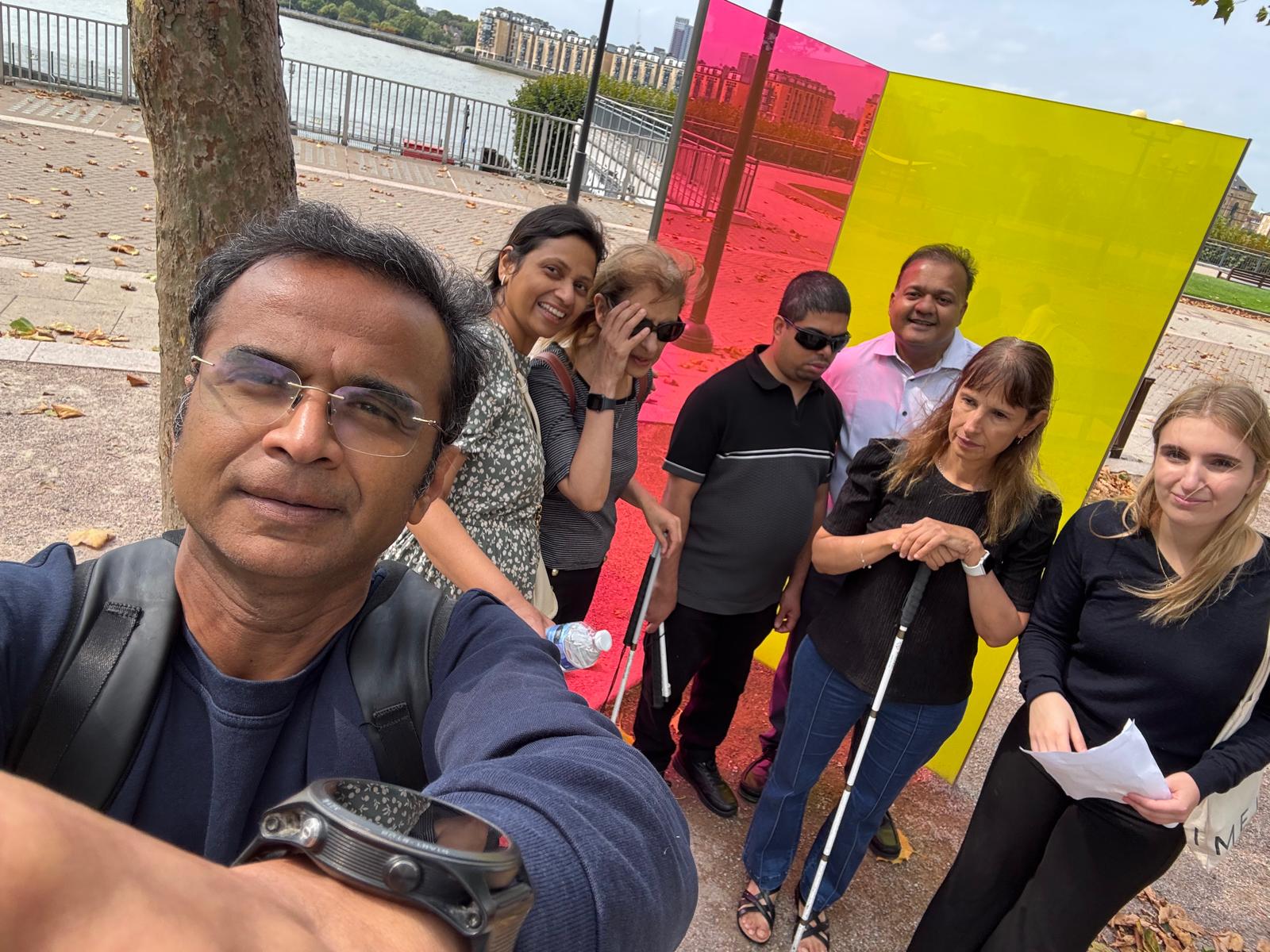 Group of VIPs and Volunteers standing in front of an art work. Deepak is taking a selfie