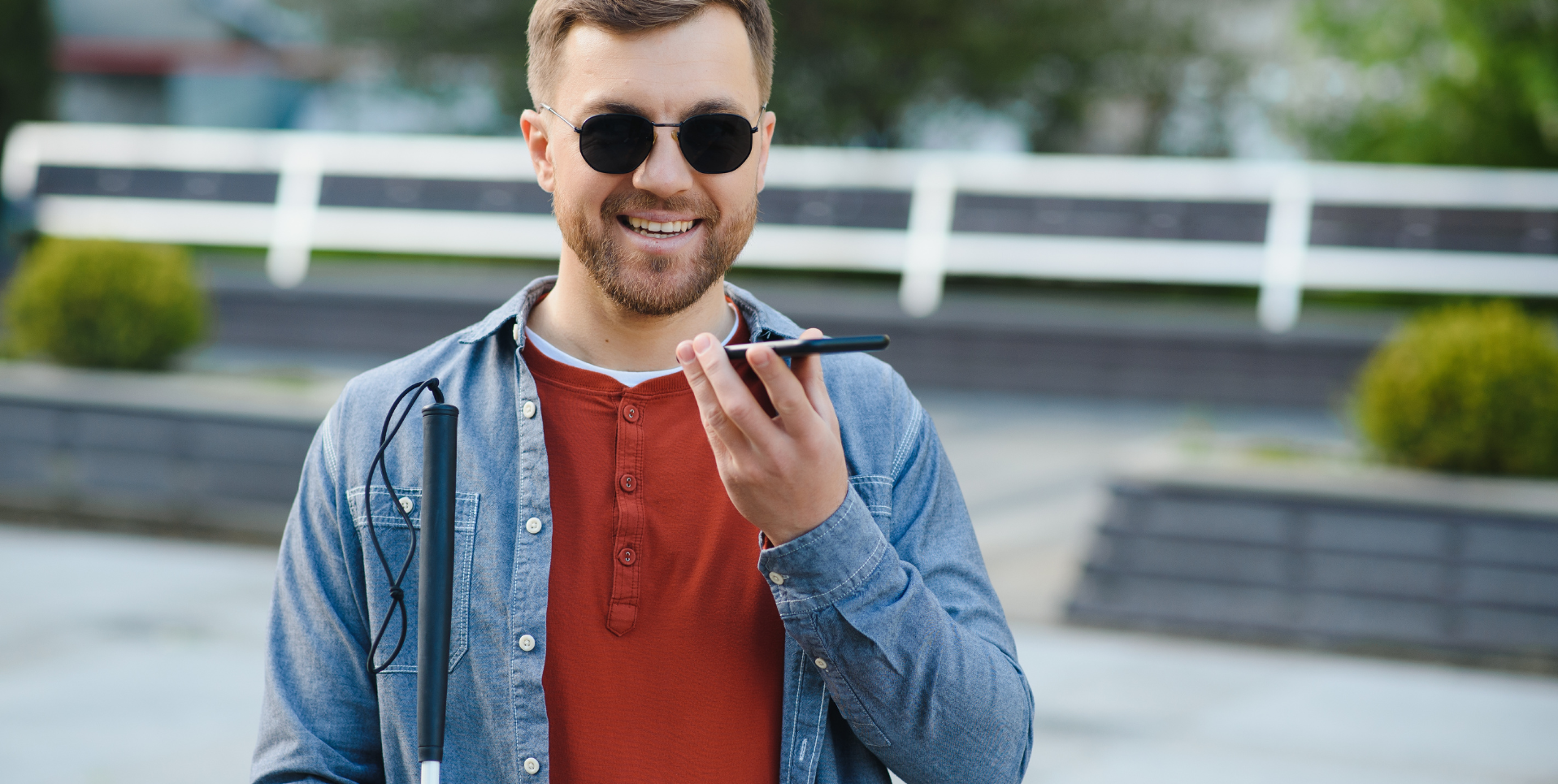 Visually impaired person using iPhone voice assistance while holding a white cane outdoors