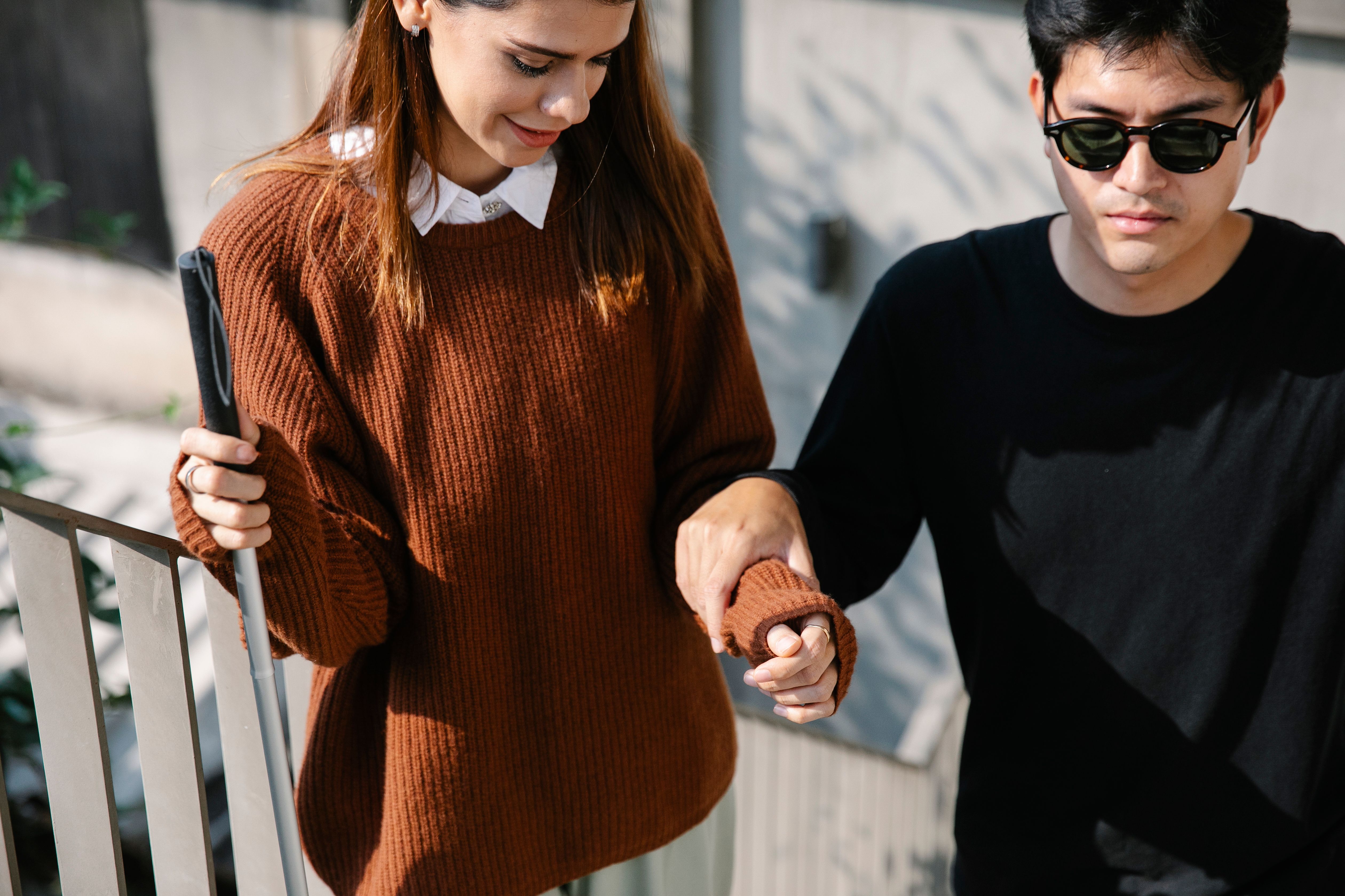a girl assissting a visual impaired person walk up the stairs