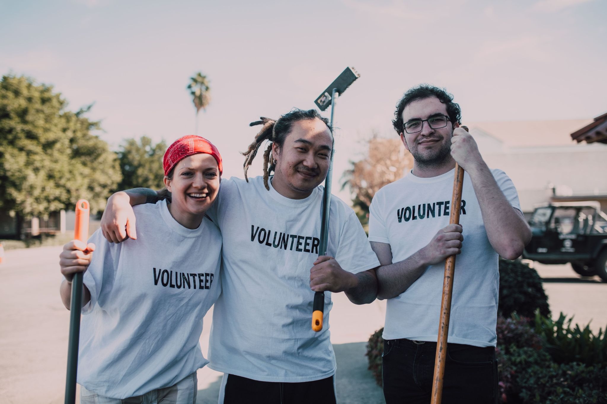 three people , wearing tees with 'volunteer" written on them, they all are smiling and volunteering for a good cause