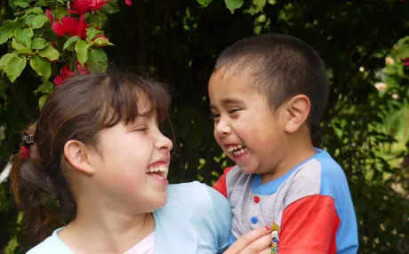 A happy young girl carries a laughing boy.