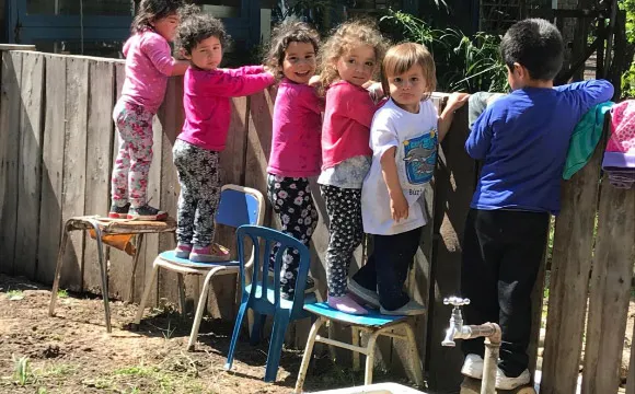 Young children standing on chairs  look over the garden fence.