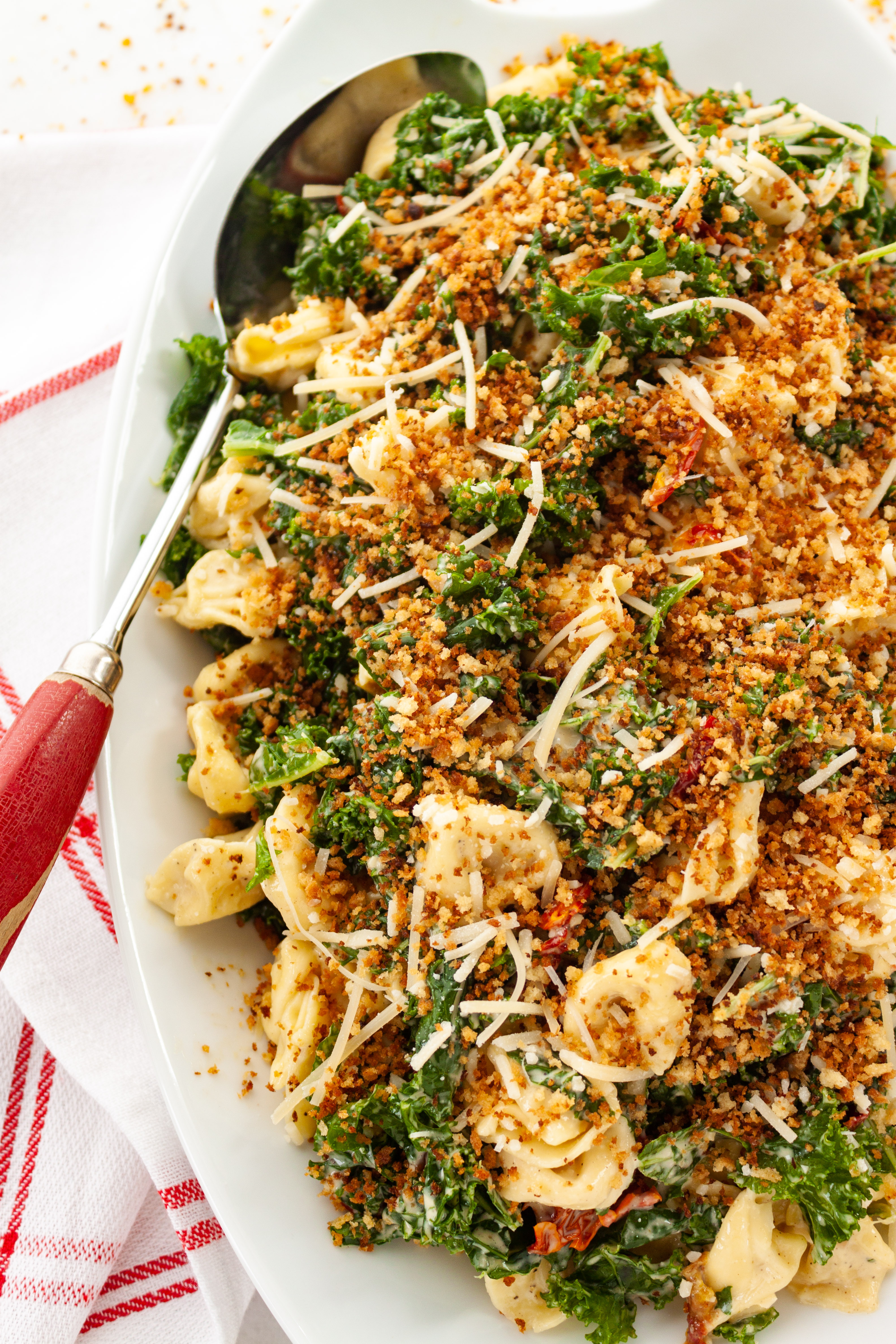 Kale Caesar Tortellini Salad on a white platter with a large serving spoon