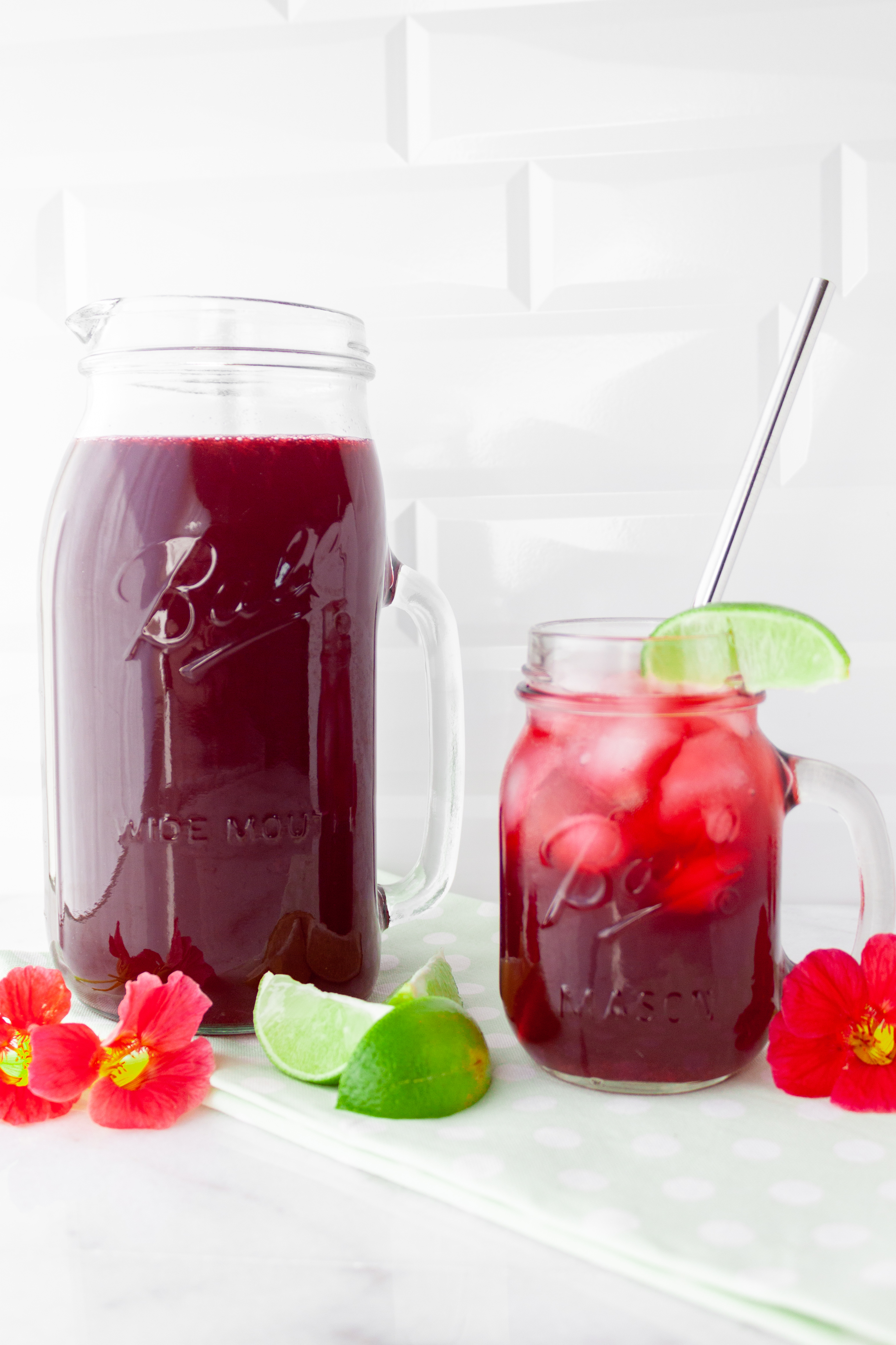 Bright red Hibiscus Limeade in a mason jar pitcher and smaller mason jar glass