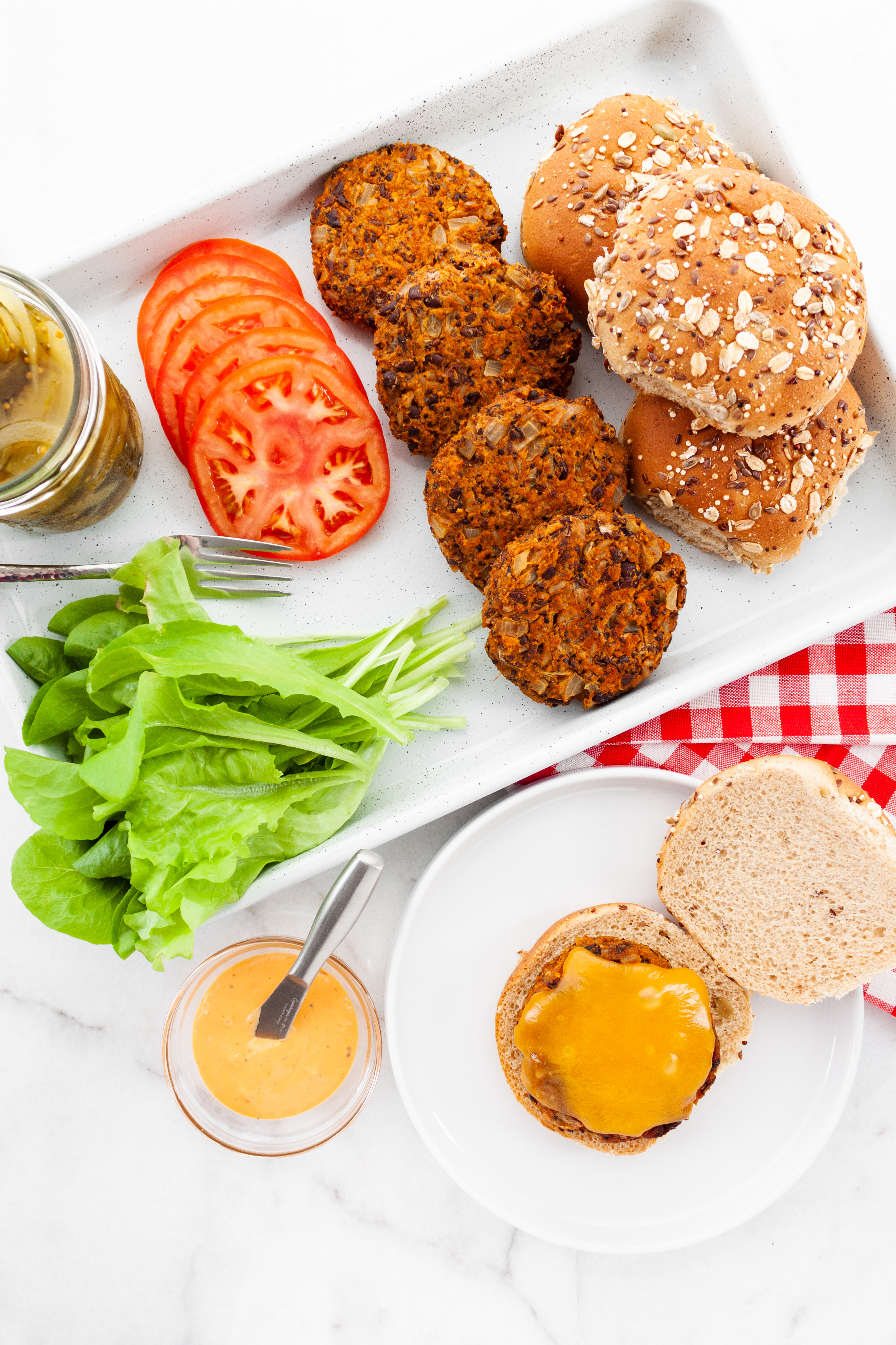 Burgers laid out with all the fixings, lettuce, tomato slices, pickles, buns 
