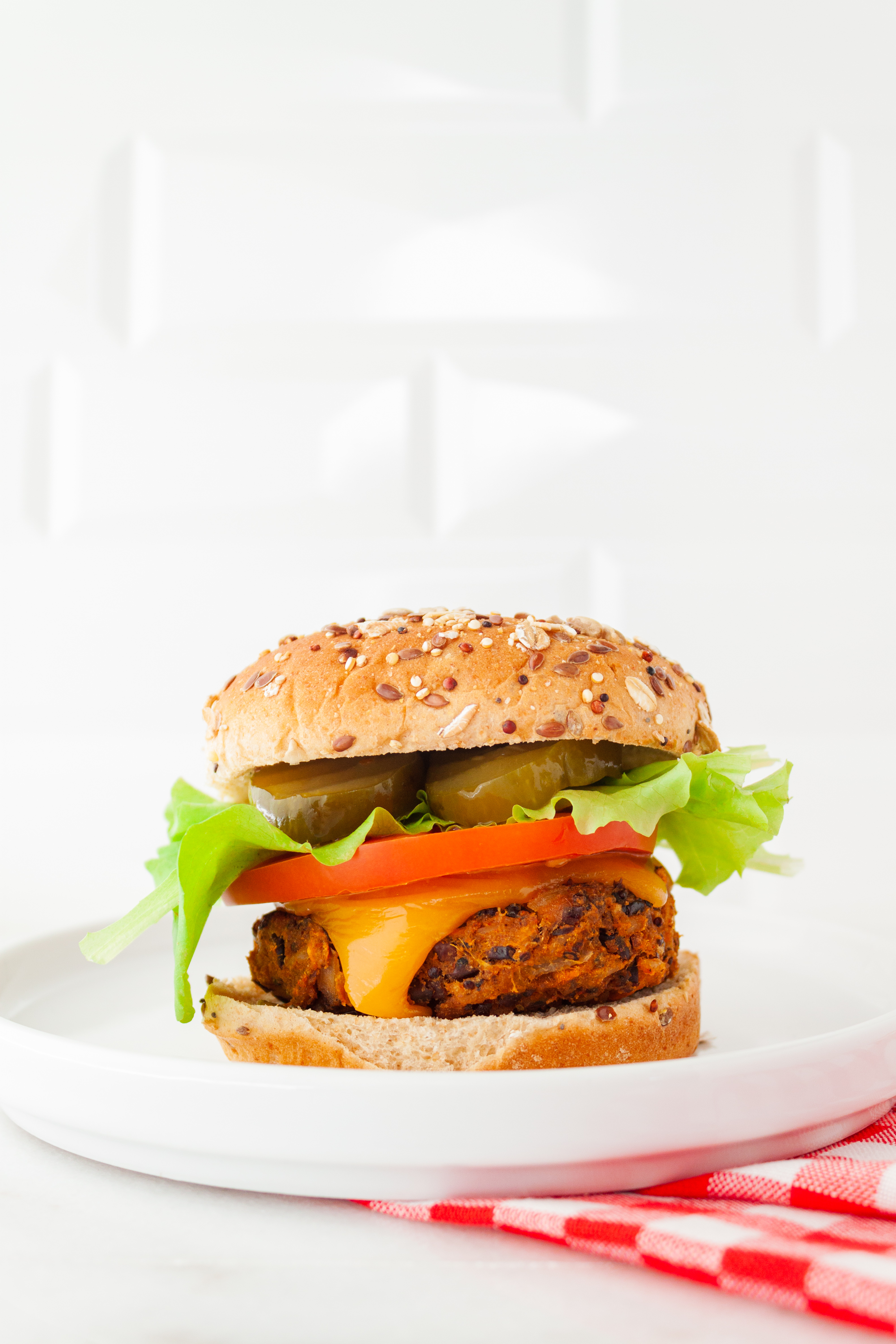 Side view of a plated veggie burger on a bun stacked with tomato, lettuce, and pickles