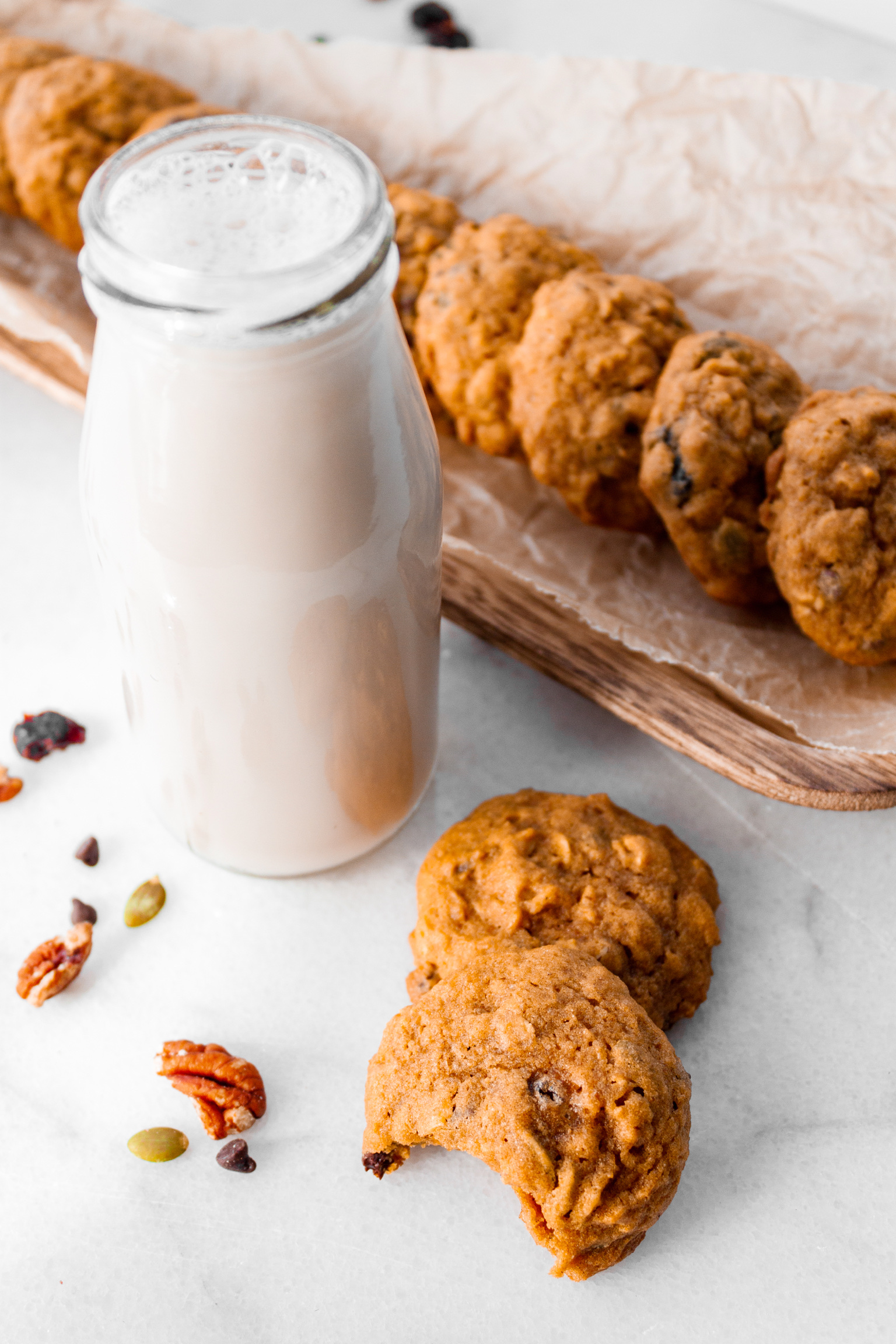 Two cookies, one with a bite taken out, with a small bottle of milk next to them