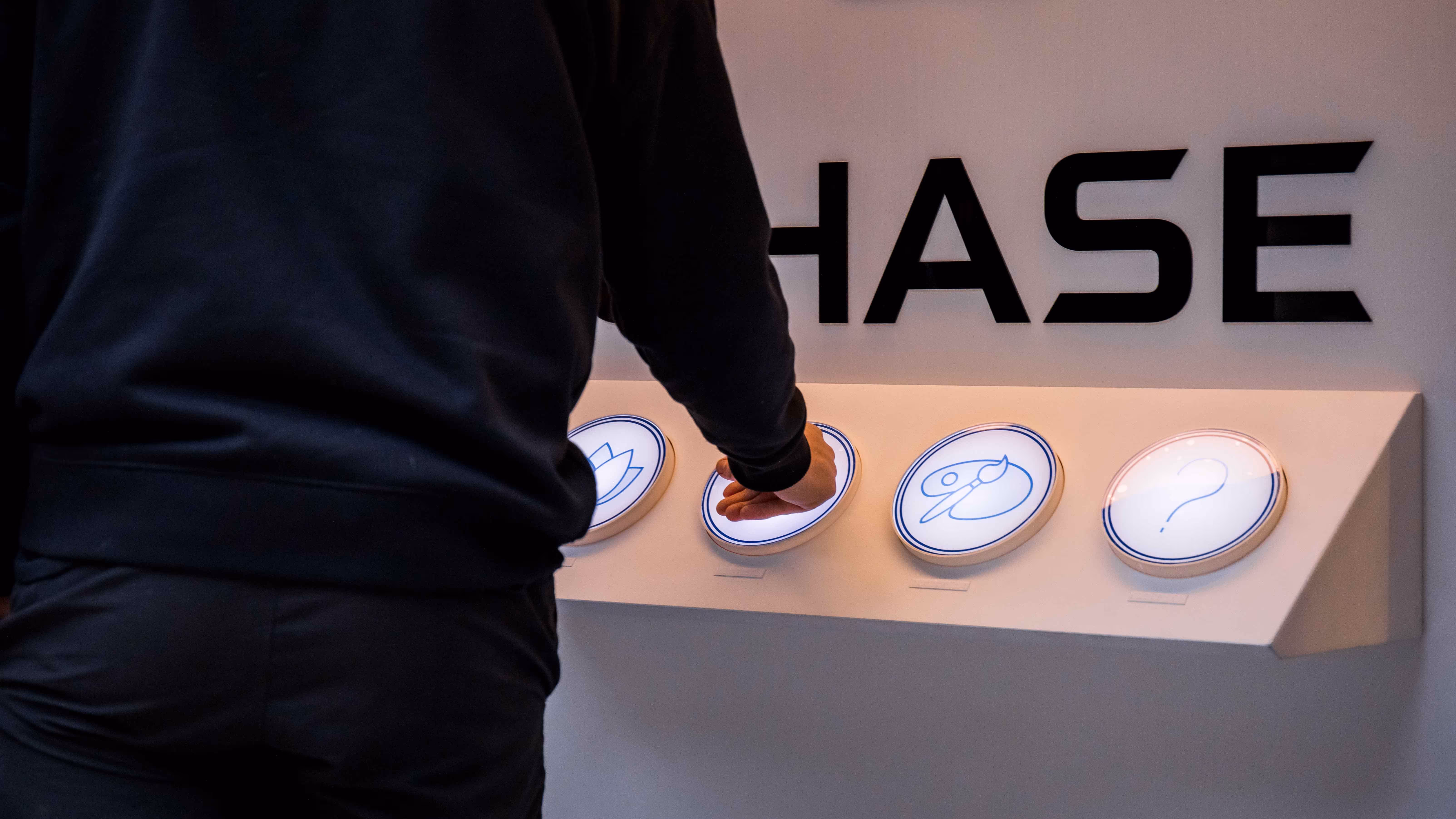 Chase bank interactive console, with person pushing large lit up buttons with logo behind. 