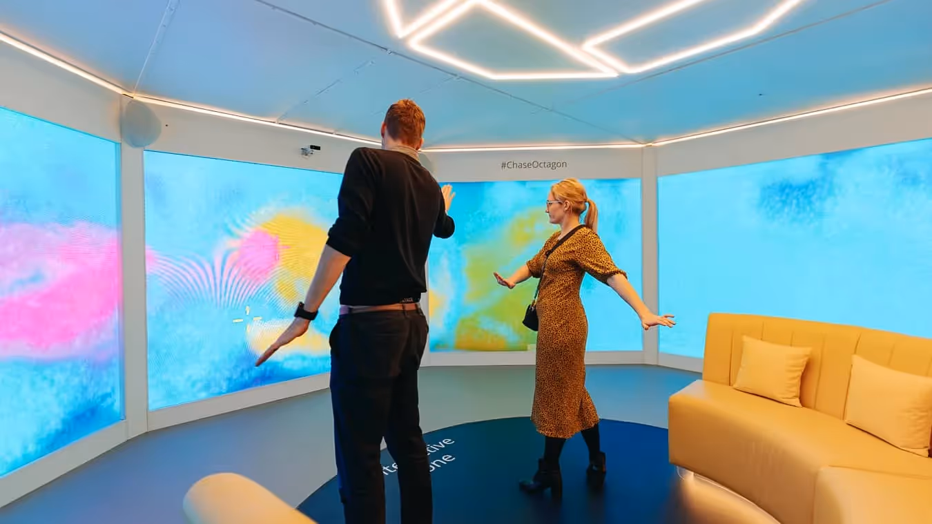 Two people inside the Chase Octagon, with four large interactive screen in front of them.