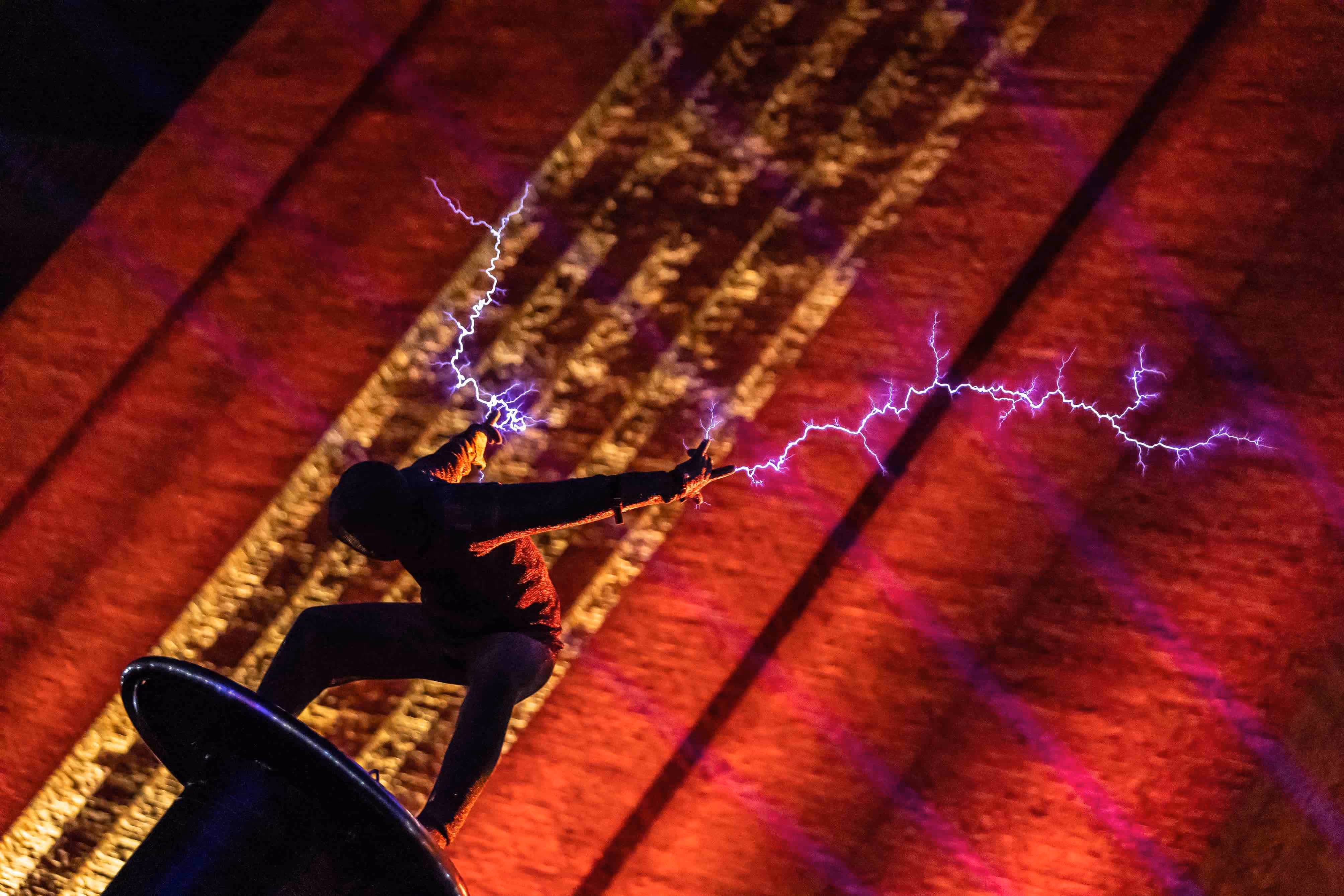 A performer stands on a plinth above the crowd at the Battersea Power Station launch event, with electric lightning coming from their hands.