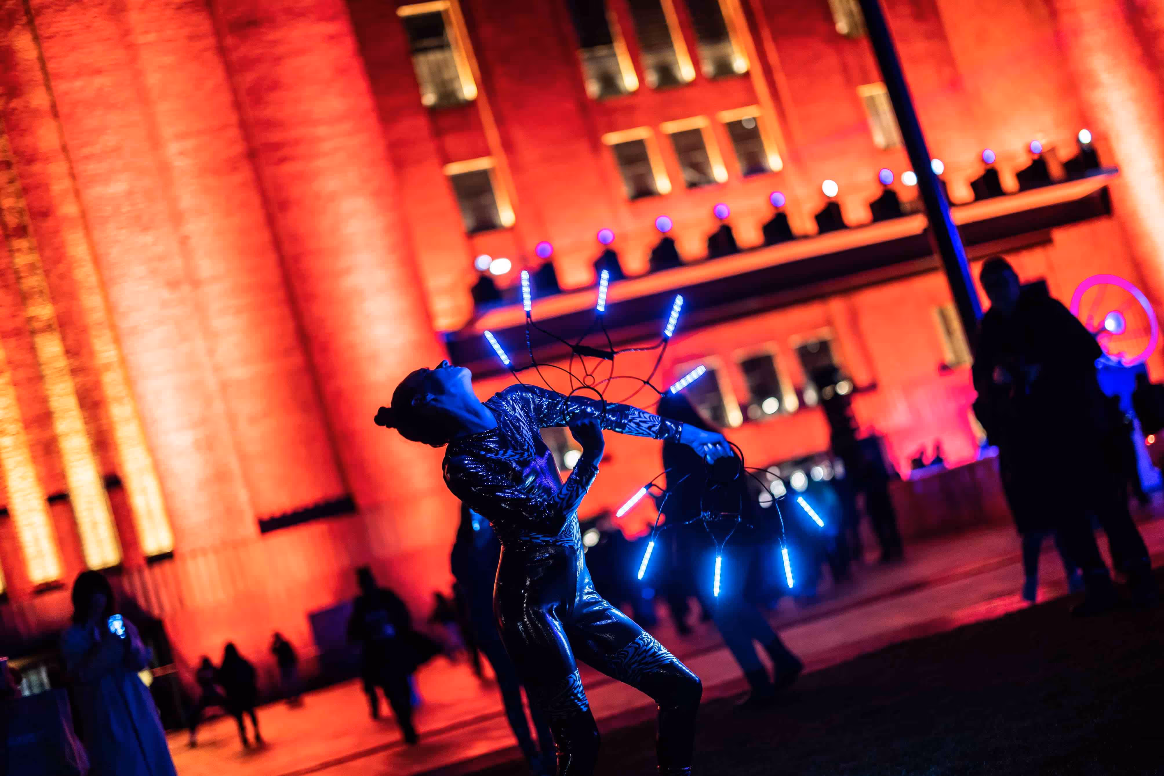 Dancers with hand-held mandalas that feature neon lighting perform in front of Battersea Power Station