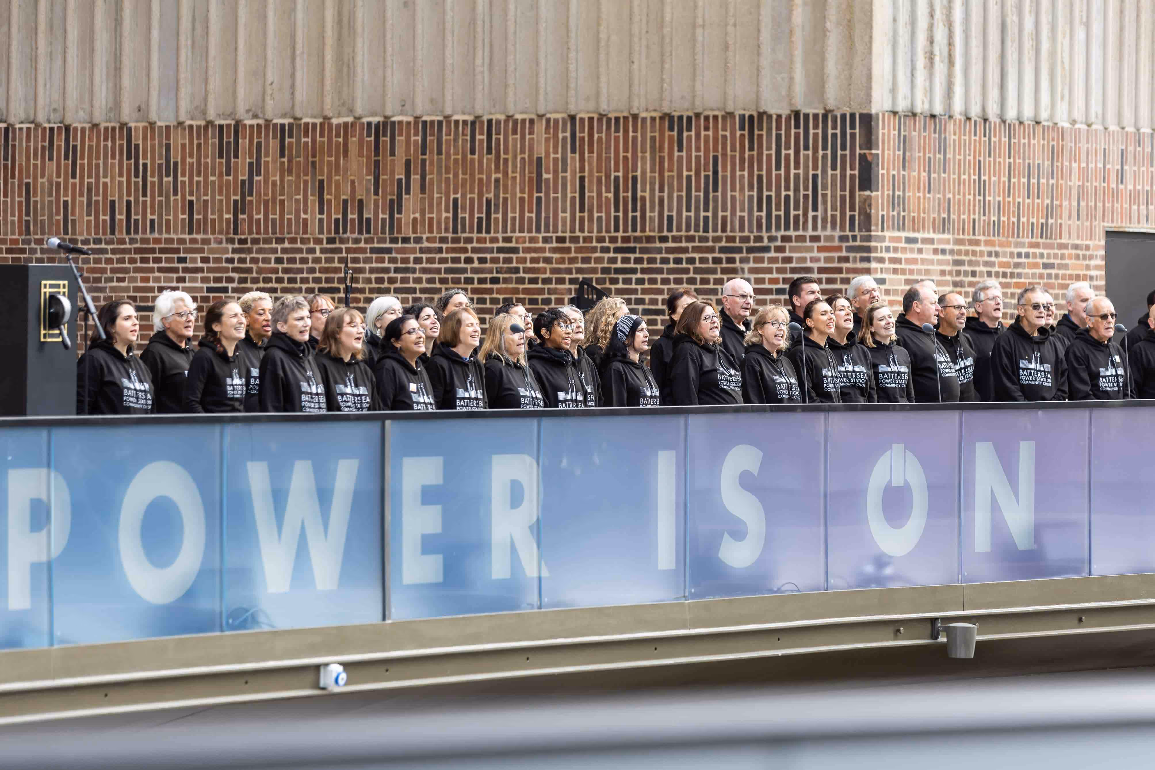 Battersea Power Station Community choir perform in fron of a sign that reads "the power is on" at the iconic Battersea Power Station opening ceremony.