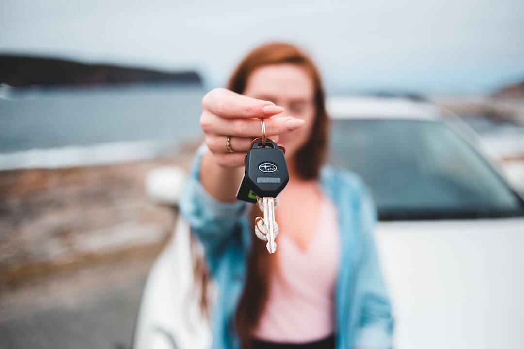 A woman sitting on a car holds up a pair of car keys