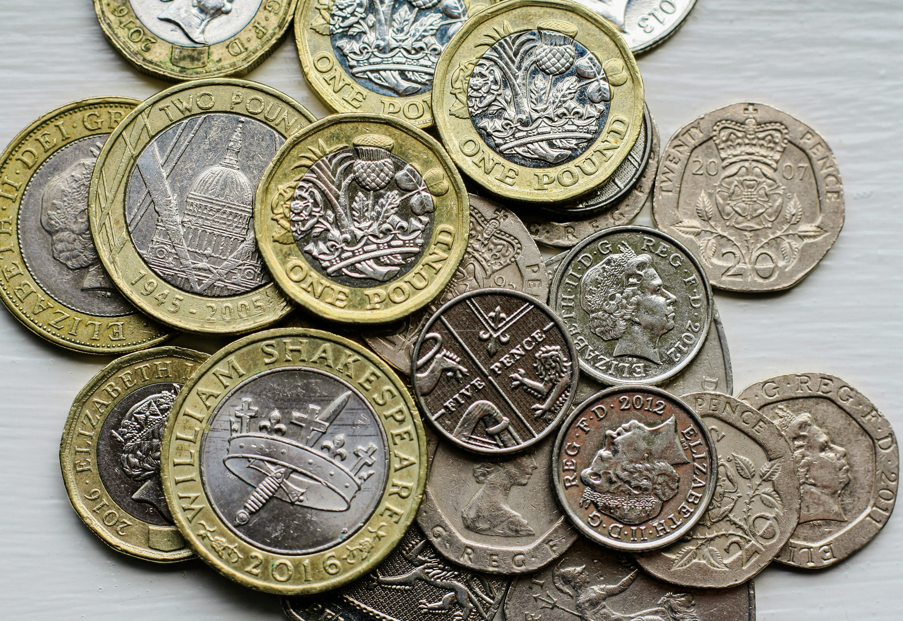 A close-up spread of various UK coins, including £1, £2, 20p and other denominations, arranged in a scattered pile.
