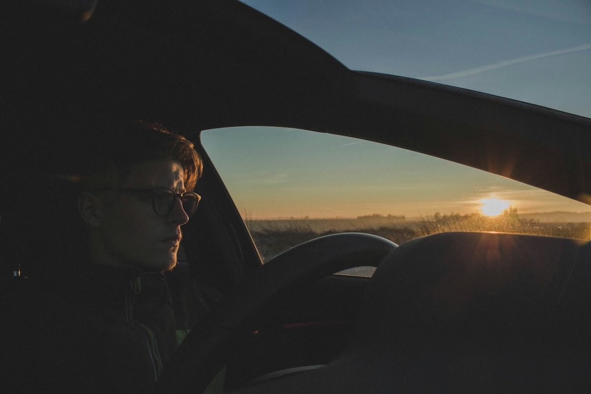 Person driving a car at sunset with sunlight streaming through the window.