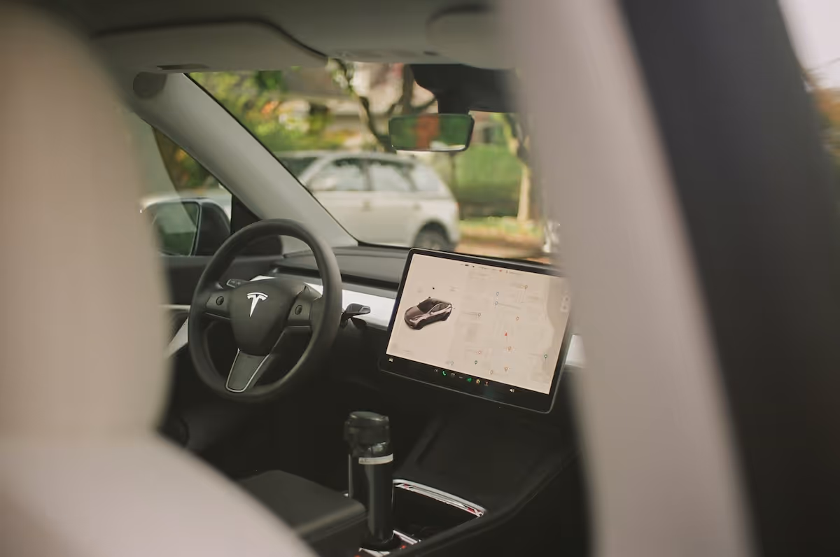  Interior of a Tesla car showing the steering wheel and central touchscreen with a navigation map displayed.
