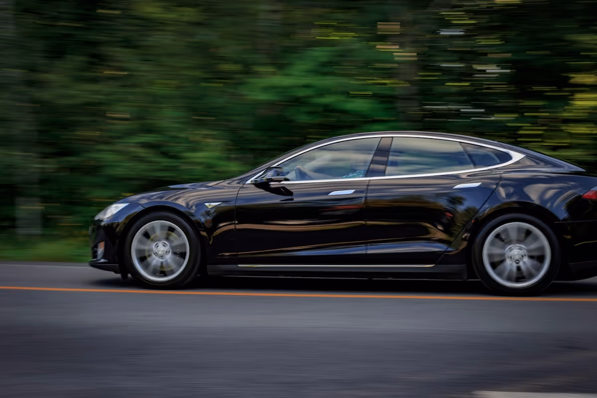 Black electric car driving along a road with motion blur against a green, wooded background.