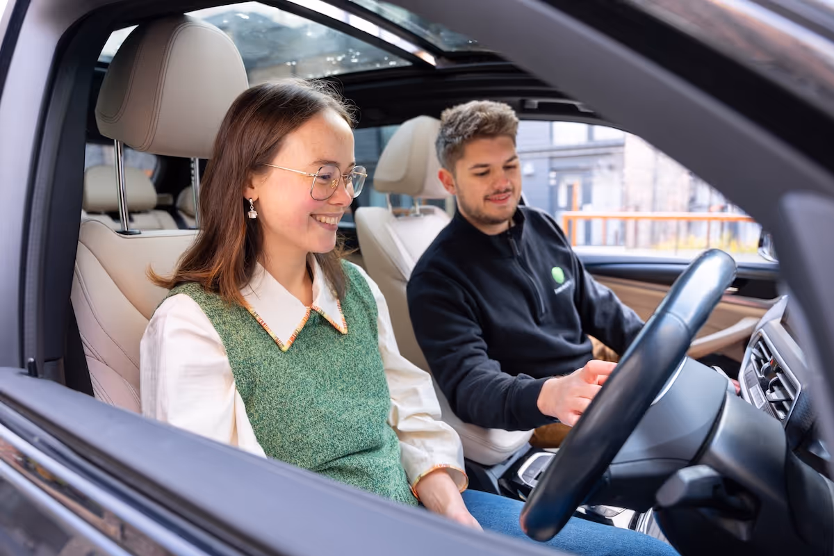 A man and woman sat in an electric vehicle smiling, looking at the dashboard