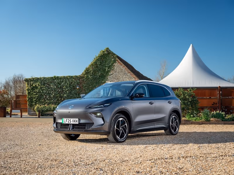 Grey electric SUV parked on a gravel driveway outside a rural building under a clear blue sky.