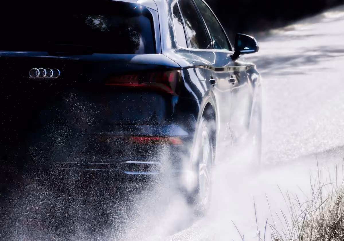A black Audi SUV drives down a road with water splashing from the wheel arches.