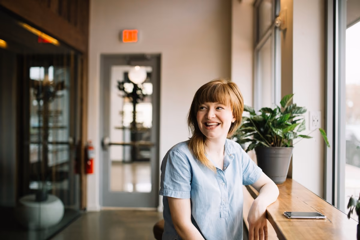 A woman sat on a stool with a big smile, clearly in a workplace