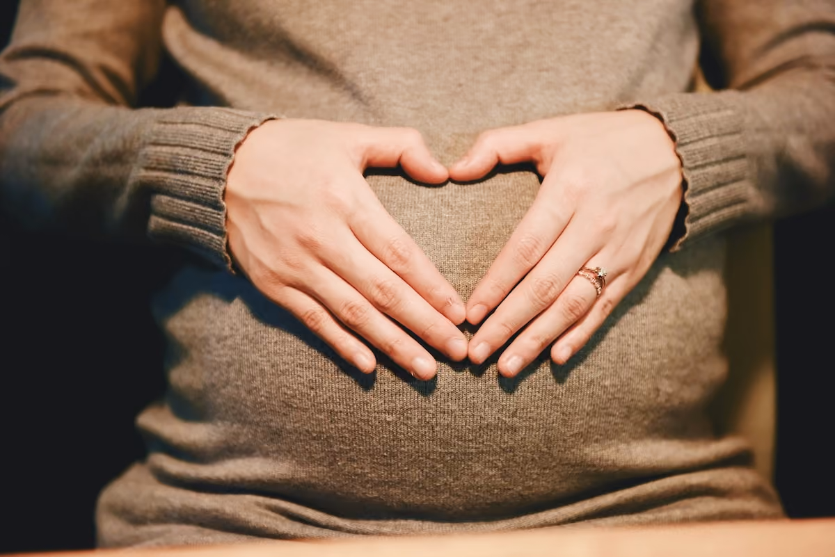 A pregnant woman with hands in a heart shape over her stomach