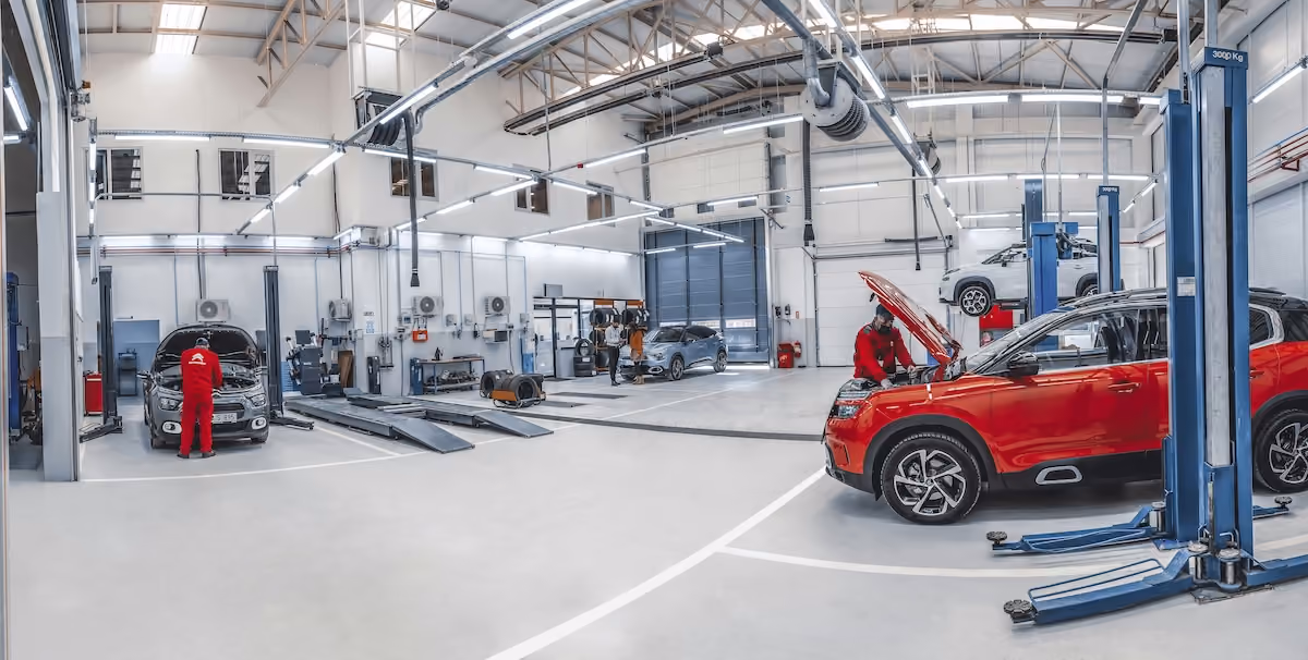 A mechanic workshop with four cars being worked on, there is one vehicle on a lift with the other 3 on ground level