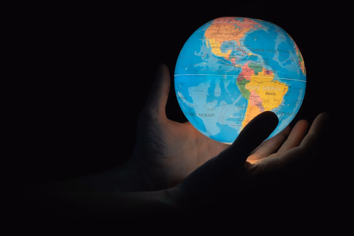 An illuminated paper globe being held by a pair of hands on a black background