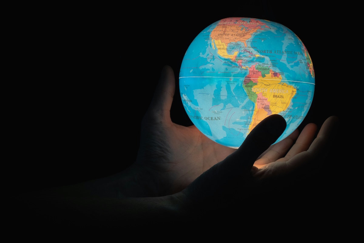 An illuminated paper globe being held by a pair of hands on a black background