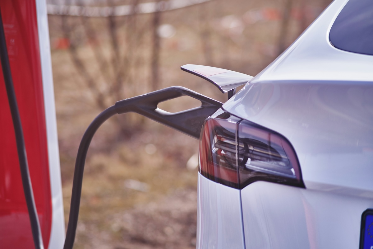 A charging cable is plugged in to the rear of a white Tesla Model 3