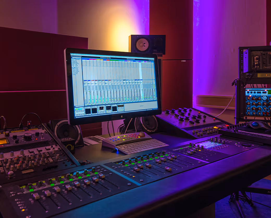 Music recording studio control room with audio mixing console, speakers, and a computer screen displaying audio mixing software.
