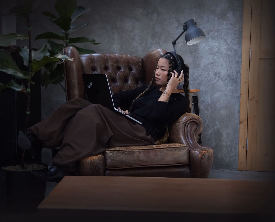 Person wearing headphones and using a laptop while sitting on a brown leather chair in a room.