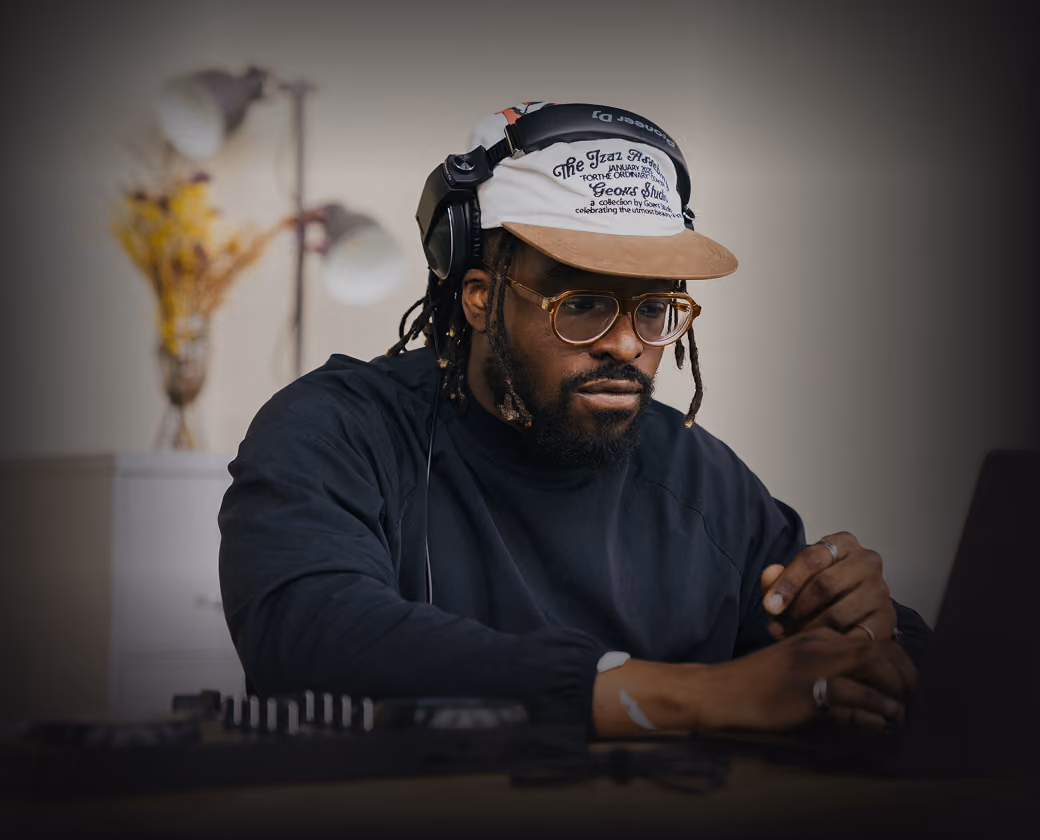 Man with glasses and cap wearing headphones working with DJ equipment indoors.