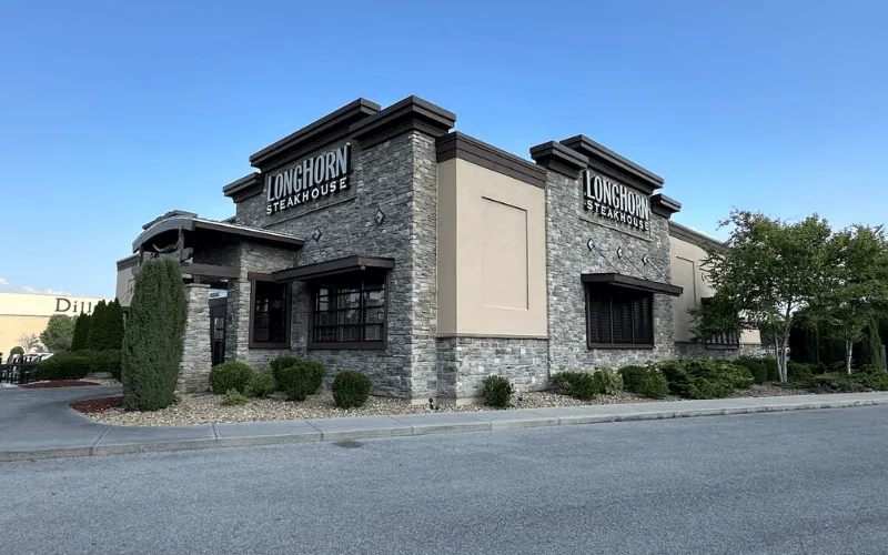 Exterior view of a LongHorn Steakhouse building with stone facade, beige walls, and landscaping under clear blue sky.
