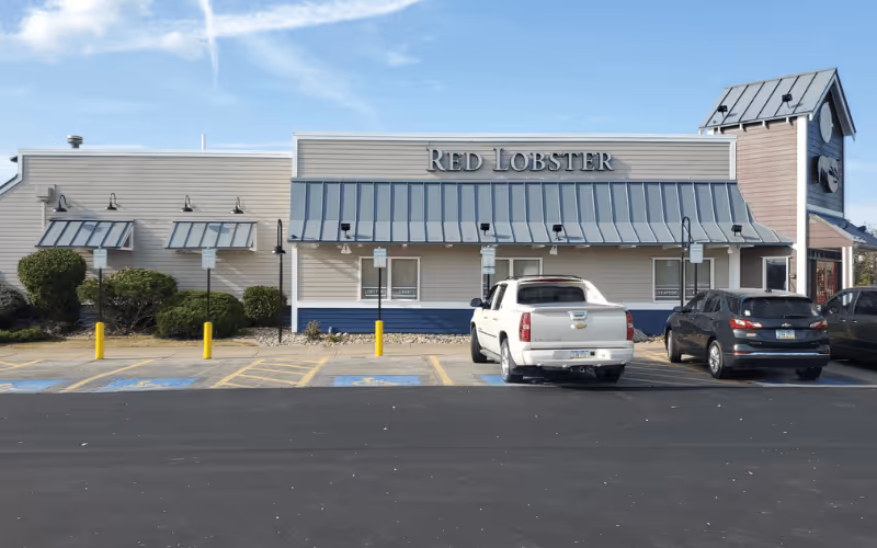 Exterior of Red Lobster restaurant with parked vehicles in front and clear blue sky.