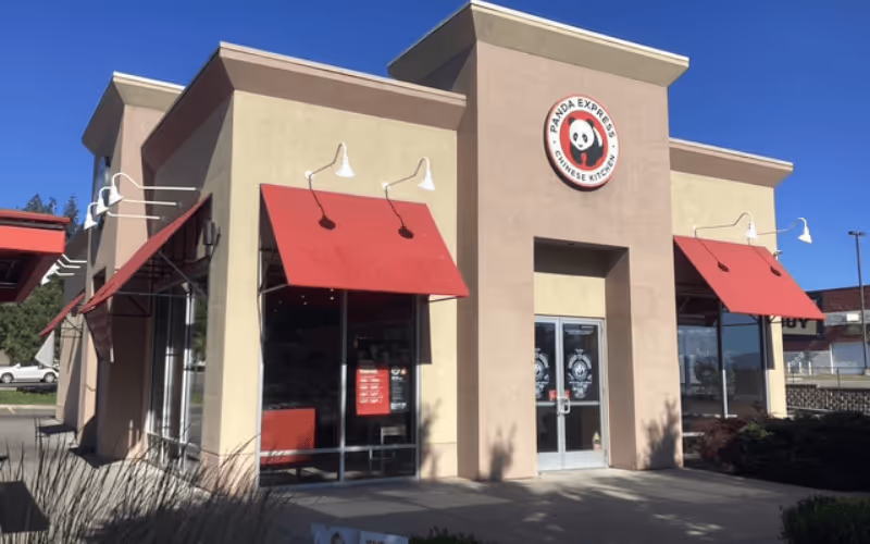 Exterior of a Panda Express Chinese Kitchen restaurant with beige walls and red awnings under a clear blue sky.